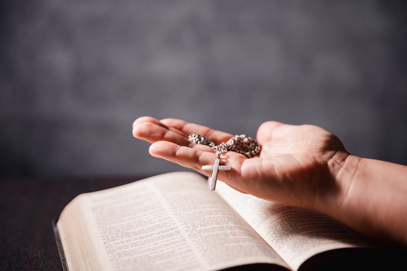 Manos sosteniendo un rosario sobre una Biblia abierta